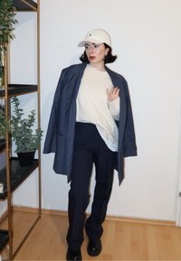 Blazer bleu marine surdimensionné, pull crème, pantalon bleu marine et bottes noires. Casquette de baseball blanche pour ajouter du contraste. Design simple et minimaliste avec des tons neutres.