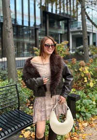 Must have musta nahkjope, millel on kunstkarusnahast krae, on kihiline beez kleit. Käes on kreemjast värvi poolkuu kujuline kott. Pruunid prillid täiendavad komplekti.