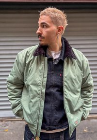 Roheline bomber-tüüpi jakk musta kunstkarusnahast kraega, esikinnitusega lukk ja taskud; kantud tumesinise teksajaki peal; kihiline välimus.