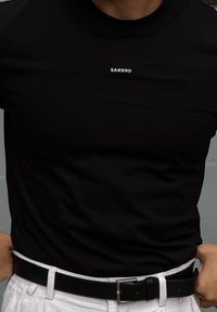 Černé bavlněné tričko s kulatým výstřihem a bílým logem "SANDRO" na hrudi, doplněné bílými kalhotami a černým páskem.