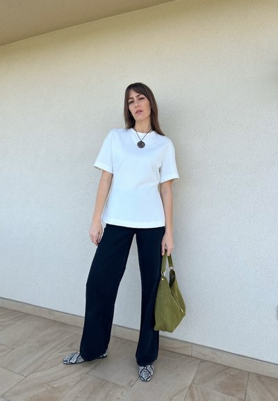 Top blanco de manga corta, pantalones negros de pierna ancha, bolso de ante verde y zapatos con estampado de serpiente. Tela suave, diseño casual.