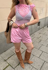 Rózsaszín csipkeblúz, ami egy szürke bralette-re van rétegezve, rózsaszín sorttal párosítva. A modellen barna velúr térdcsizma és több fém gyűrű látható.