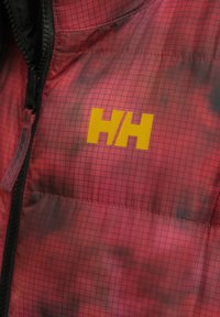 Κόκκινο ραφτό μπουφάν με καρό σχέδιο, μαύρο φερμουάρ και εξέχον κίτρινο λογότυπο "HH" στο στήθος.