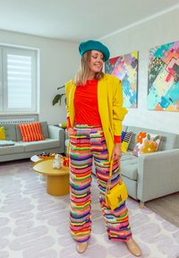 Knallgelber übergroßer Blazer, rotes Langarmshirt, bunt gestreifte, weit geschnittene Hose, petrolfarbener Barett und eine gelbe Handtasche mit Kettenriemen.