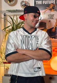 Bílý síťovaný dres Nike s námořnickými akcenty, krátké rukávy, s velkým logem "NIKE" na přední straně a malou cedulkou na lemu.