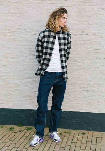 Camisa de franela a cuadros blanco y negro sobre una camiseta blanca, combinada con pantalones de mezclilla azul y zapatillas blancas con acentos morados.