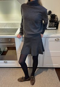 Grauer Strick-Turtleneck-Pullover, grauer ausgestellter Rock, schwarze Strumpfhosen und Loafers mit Leopardenmuster. Glatte Textur, lässiges Design und figurbetonter Stil.