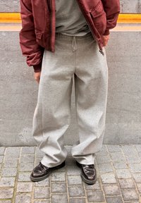 Pilkos laisvalaikio kelnės su laisvu siluetu, raišteliu juosmenyje ir minkštu audiniu, derinamos su tamsiai ruda avalyne ir bordo spalvos bombonešio striuke.