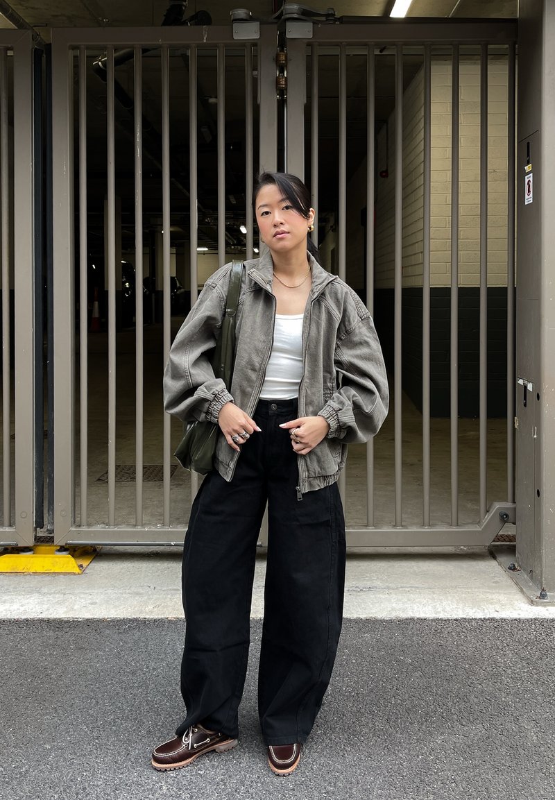 Veste matelassée grise courte avec manches bouffantes, débardeur blanc, pantalon large noir, et chaussures bateau marron. Sac vert et bijoux argentés.