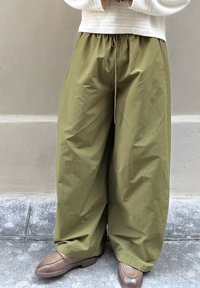 Olivgrüne, weit geschnittene Hose mit elastischem Bund und Kordelzug. Kombiniert mit braunen Lederloafern auf strukturiertem Untergrund.