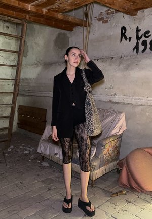 Blazer negro, top corto negro, leggings de encaje, sandalias de plataforma gruesa. Bolso de hombro con estampado. Habitacion de colores neutros con escalera de madera.