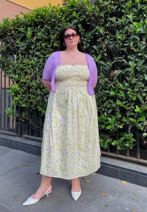 Vestido largo floral en amarillo y blanco con corsé fruncido, combinado con un cárdigan morado suave. Llevado con tacones tipo slingback blancos.