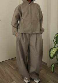 Sweat à capuche gris zippé avec une capuche, associé à un pantalon de survêtement gris ample. Confectionné dans un tissu doux et texturé, avec des poches latérales.