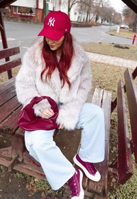 Γκρίζα ψεύτικη γούνα μπουφάν, ανοιχτό μπλε παντελόνι σε φαρδιά γραμμή, μπορντό αθλητικά παπούτσια και τσάντα με υφή σε ταιριαστό χρώμα. Κόκκινο καπέλο με λευκό λογότυπο. Εξωτερικός χώρος.