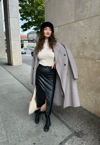 Hallü grau villane gavil, sobiv beež turtleneck, must nahkne seelik koos lõhega ja mustad nööpidega saapad. Viib käes väänatud kreemivärvi käekoti.