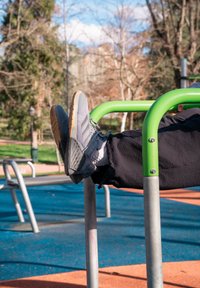 Chaussures de sport grises à surface texturée et semelles en caoutchouc reposant sur une barre d'exercice verte, sur un sol de terrain de jeu en caoutchouc bleu.