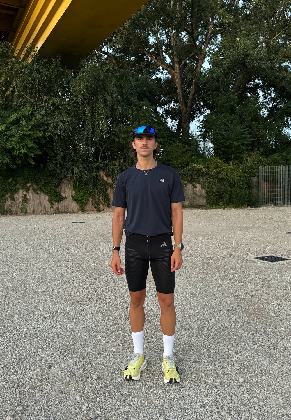 Sportig outfit med en mörkblå t-shirt med kort ärm, svarta shorts med ränder, vita strumpor och gula sneakers. Blå spegelglasögon ingår.