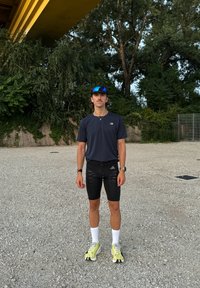 Sportig outfit med en mörkblå t-shirt med kort ärm, svarta shorts med ränder, vita strumpor och gula sneakers. Blå spegelglasögon ingår.