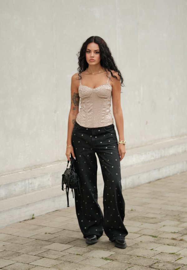 Top bej cu corset, cu un model texturat, asortat cu blugi negri cu picioare largi, având accente metalice. Accesoriu: geantă mică neagră.