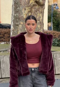 Casaco de peluche burdeos com gola larga, combinado com um top cropped marcante e jeans escuros de cintura alta. Tecido suave e silhueta ajustada.