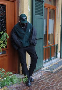 Giacca a vento verde indossata sopra un cardigan verde e una maglietta nera, abbinata a pantaloni cargo neri e stivali neri massicci.