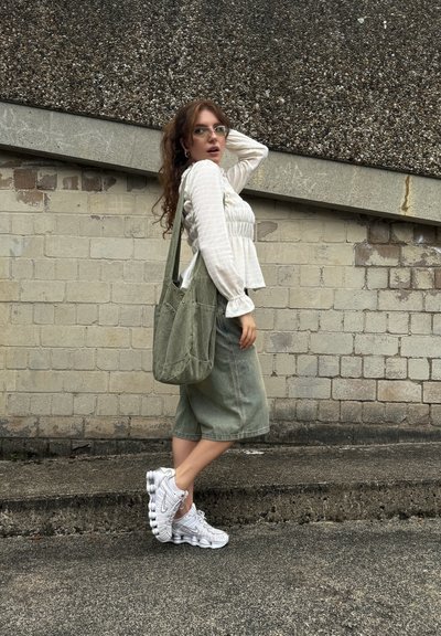 Top blanco ligero de manga larga con rayas texturizadas, pantalones cortos de mezclilla verde y un bolso verde de hombro. Combinado con zapatillas blancas texturizadas.