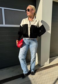 Μαύρο και άσπρο κοντομάνικο κασκόλ σε χρώματα με δύο μπροστινές τσέπες και ασημένια κουμπιά, συνδυασμένο με ανοιχτό μπλε ίσια παντελόνια και κόκκινο κοστούμι.