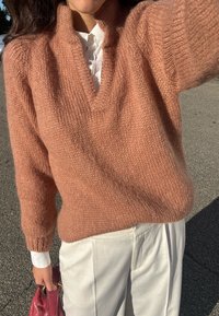 Miękki, luźno dopasowany sweter w odcieniu różowego nalewu z dekoltem w kształcie litery V oraz fakturowanym splotem, zestawiony z białymi spodniami o kroju dopasowanym oraz małą bordową torebką.