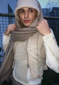 Μπεζ τζιν γιλέκο πάνω από μια υφασμάτινη λευκή μπλούζα, ριγμένο με ένα ανοιχτό καφέ μαντήλι. Μια μαλλινή μπεζ καπέλο προσθέτει ζεστασιά, συνοδευόμενο από ασημένιες δαχτυλίδια.