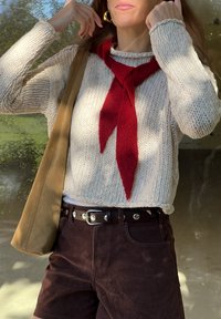 Gebreide crèmekleurige trui met rode sjaaltje, bruine suède shorts en een tan tas. Heeft een gestructureerde stof en een casual, gelaagde uitstraling.