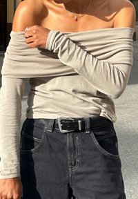 Μπεζ τοπ με ανοιχτούς ώμους και μακριά μανίκια, υφασμάτινη υφή, συνδυασμένο με σκούρες τζιν παντελόνες με αντίθετη ραφή και μαύρη ζώνη.