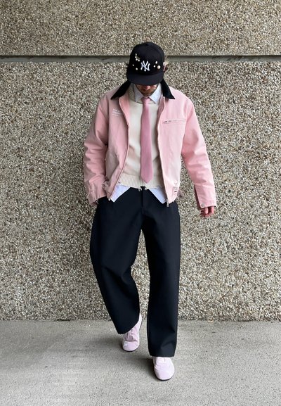 Chaqueta rosa con cuello negro, suéter blanco y pantalones de pierna ancha negros; zapatillas rosas; gorra negra con logo blanco y adornos.