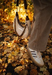 Pantalones de pana marrones, zapatillas Adidas Gazelle blancas pisando hojas de otoño y un bolso de piel de oveja beige con cadena de carey.