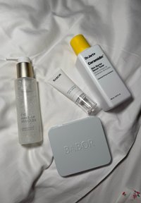 Vier Hautpflegeprodukte: eine durchsichtige Flasche mit einer goldenen Pumpe, beschriftet mit "Babor Augen Make-up Entferner", eine weiße Tube mit dem Aufdruck "Babor Augenserum", eine weiße Flasche mit einem gelben Deckel, beschriftet mit "Dr.Jart+ Ceramidin Hautbarriere Serum Toner", und ein graues Kompakt mit eingeprägtem "Babor".