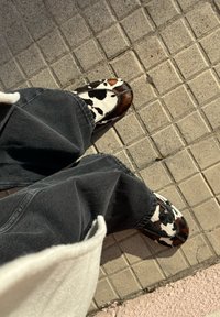 Lehmustäpiliste pruunide ja valgete mustritega klotsid, millel on tekstuuriga karvataoline pind, neid kantakse lahtiste tumedate hallide teksadega.