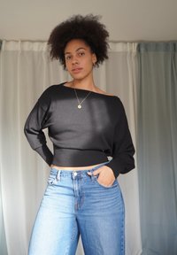 Maglione nero a maglia con scollo a barca, maniche lunghe e orlo a coste, abbinato a jeans a gamba larga a vita alta di colore azzurro chiaro.