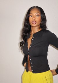 Haut noir à manches longues avec fermeture par boutons et coupe ajustée, associé à un pantalon jaune vif à cordon, présenté sur un fond neutre.