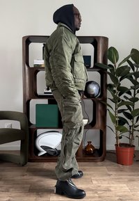 Veste bomber vert olive avec poignets côtelés et poches poitrine associée à un pantalon cargo ample. Bottines noires à fermeture éclair latérale et talon épais.