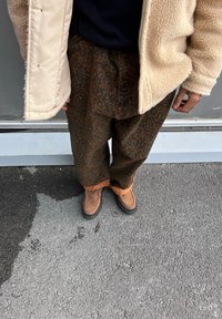 Καφέ παντελόνι με λεοπάρ μοτίβο και πορτοκαλί μανσέτα, συνδυασμένο με καφέ μπότες μέχρι τον αστράγαλο. Το εξωτερικό ρούχο είναι μια κρεμ υφή, φλις παλτό.