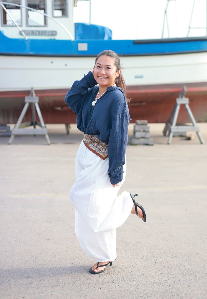 Pantaloni bianchi fluidi abbinati a una maglietta a maniche lunghe blu scuro. Una cintura con motivo valorizza il punto vita. Infradito nere completano l'outfit.