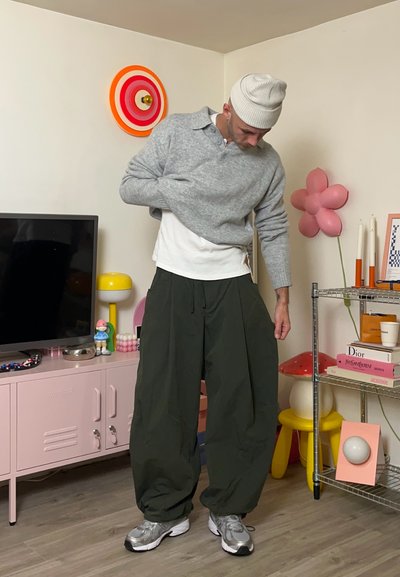 Suéter de punto gris sobre una camisa blanca, combinado con pantalones verdes anchos y zapatillas grises. Decoración colorida en el fondo.