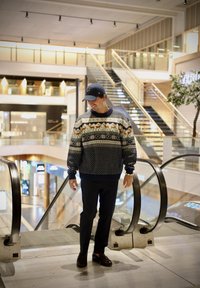 Pletena džemper s geometrijskim uzorkom u mornarskoj, krem i zemljanim tonovima; rebrasti ovratnik i manžeti; uparen s tamnim hlačama i smeškim cipelama.