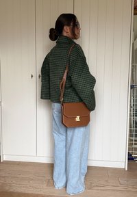 Zelená károvaná krátka bunda, svetlomodré džíny s širokými nohavicami, hnedá crossbody kabelka so zlatým kovaním, doplnené slnečnými okuliarmi.