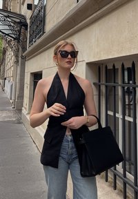 Zwarte haltertop blazer, getailleerd, met een enkele knoop, gecombineerd met lichtblauwe wijdere jeans. Geaccentueerd met een zwarte handtas en zonnebril.