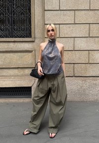 Halter neck-top i grått med kamouflage mönster; vida, olivgröna byxor; liten svart handväska; flip-flops; urbant bakgrund med texturerad vägg.