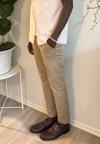 Pantaloni beige su misura, abbinati a mocassini marrone scuro e una camicia a righe verticali rosa chiaro. Tessuto morbido e design aderente.