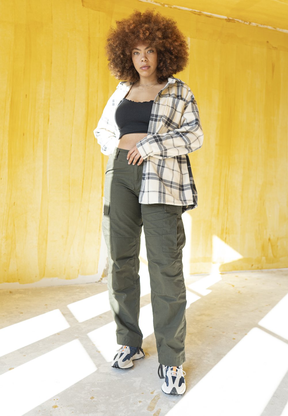 Geruite, lange mouw blouse in beige en zwart, zwarte crop top, groene cargobroek, en sportieve schoenen met een gestructureerde, gelaagde zool.