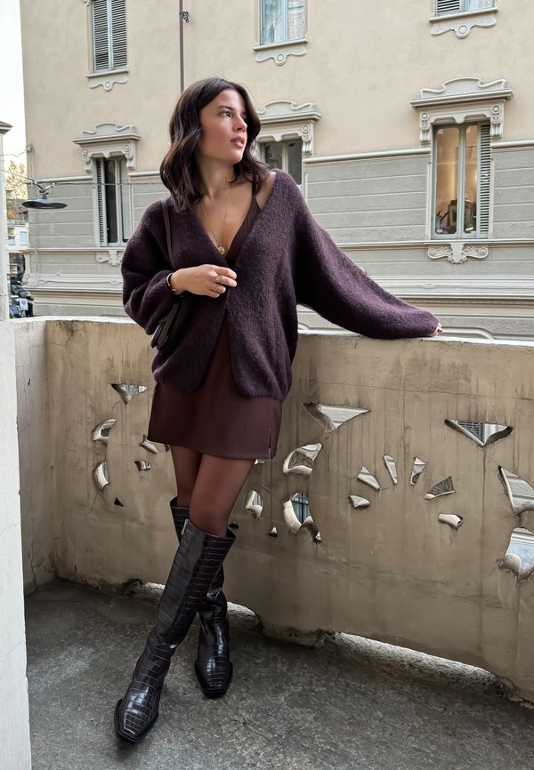 Yarnika maroon oversized, bertekstur dipakai di atas gaun cokelat, dipadukan dengan sepatu bot kulit croc-embossed berwarna cokelat tua hingga lutut.