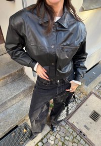 Giubbotto corto in pelle nera con chiusura a bottoni, tasche frontali, abbinato a jeans neri a vita alta e una borsa con stampa zebra.