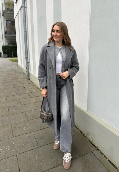 Abrigo de lana gris, suéter gris claro, jeans de mezclilla de cintura alta y zapatillas grises. Incluye un pequeño bolso gris con detalles de herraje.